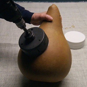 person cutting a hole into a dried kettle gourd